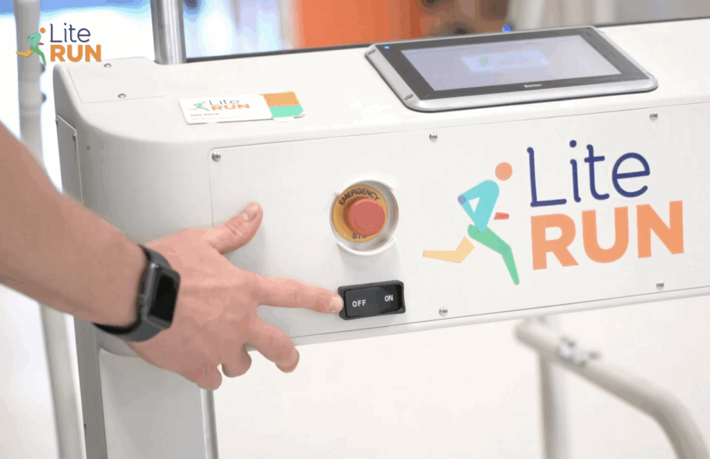 A physical therapist's hand about to push the on/off switch on a Lite Run mobility trainer to start a therapy session