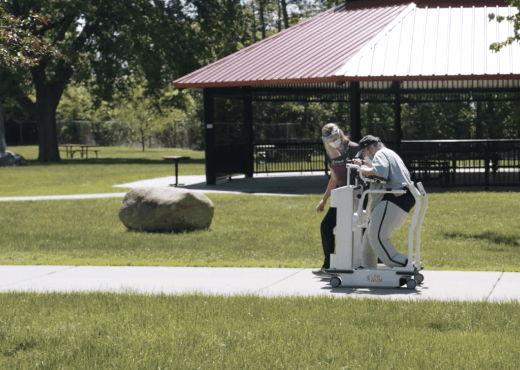 A veteran and a physical therapist walking outside in a park for therapy using a Lite Run mobility trainer